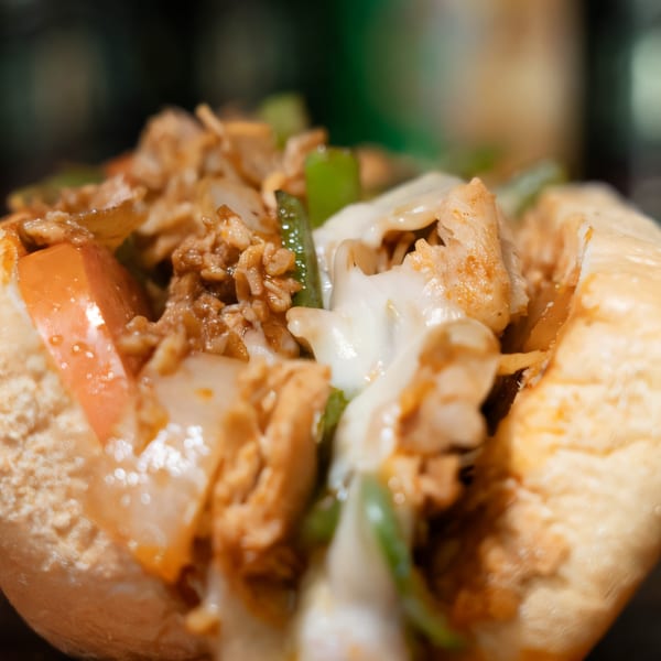 Close-up of a Mojo's cheesesteak, filled with meat, melted cheese, green peppers, and onions.