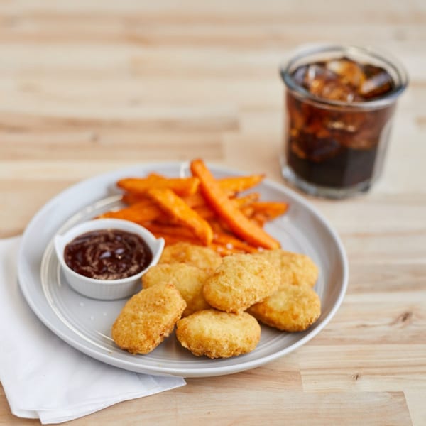 Mojo's chicken nuggets, sweet potato fries, BBQ sauce, and a soda on a wooden table.